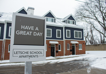 A sign says "Have a great day" in front of a few new townhomes on a snowy day.